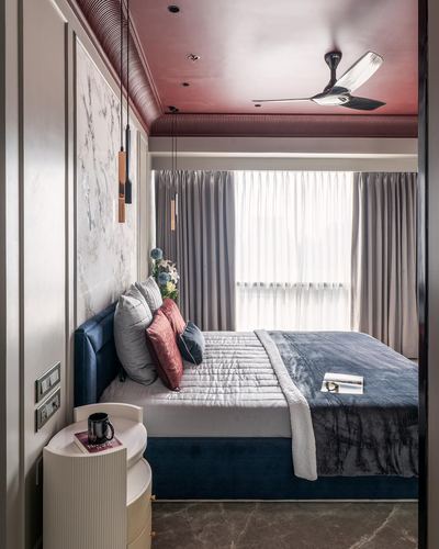 Bedroom with navy velvet bed, marble accent wall, and burgundy ribbed ceiling with pendant lights