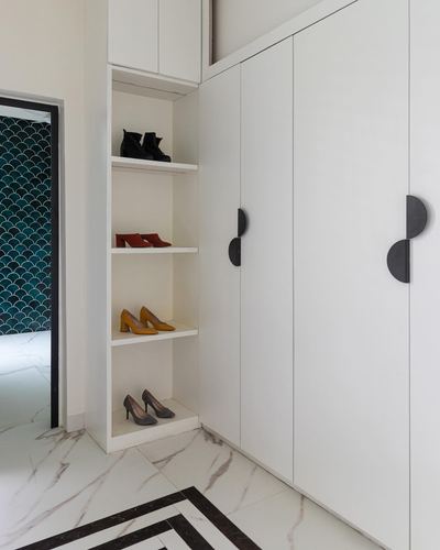 White wardrobe wall with open shoe shelves and half-moon black handles beside marble-look floor