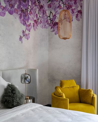 Bedroom corner with floral mural, woven pendant lamp, and mustard velvet armchair