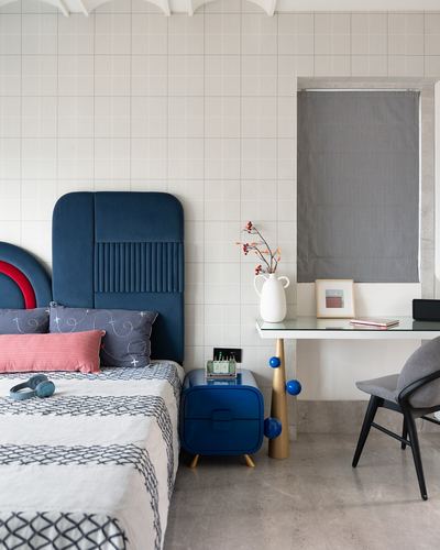 Bedroom with arched navy velvet headboard, patterned bedding, and a glass-top desk with brass legs