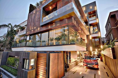 Multi-storey contemporary house facade with perforated metal screens, glass balconies, and a red car in the driveway at dusk