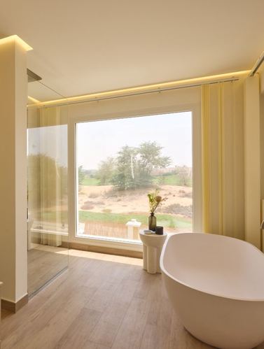 Freestanding tub beside floor-to-ceiling window overlooking desert landscape in sunlit bathroom