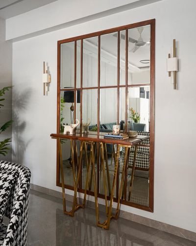 Wood-framed windowpane mirror above a brass-legged console table in a foyer