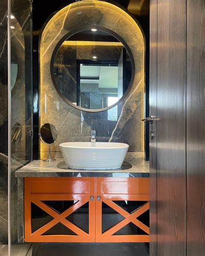 Bathroom vanity with round backlit mirror, marble-look wall, and orange cross-panel cabinet doors