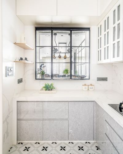 White marble kitchen with grey stone cabinetry and black-framed interior window overlooking living room