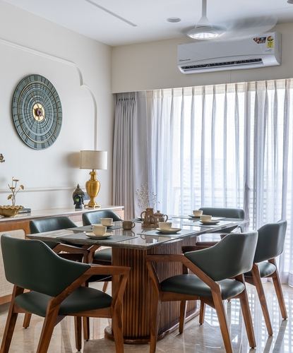 Dining room with fluted wood table, green leather chairs, and round wall art near sheer curtains