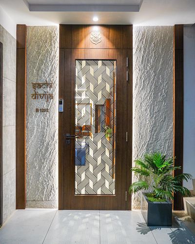 Wooden entrance door with geometric glass insert flanked by textured stone panels and a potted plant