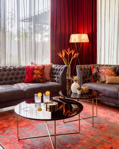 L-shaped grey tufted sofa with red velvet curtain backdrop and round glass nesting tables