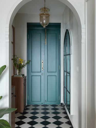 Arched hallway leading to teal panelled double doors with a glass lantern above checkerboard flooring