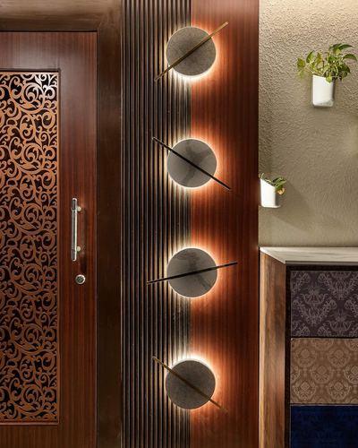 Ribbed wood panel with four backlit stone discs beside a carved wooden door and patterned cabinet
