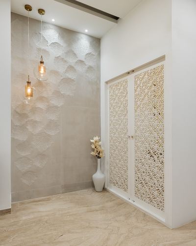 Foyer with leaf-textured stone wall, glass pendant lights, and carved white jali cabinet doors