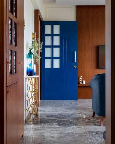 Entryway view through a glossy blue paneled door into a wood-clad living room with marble flooring.