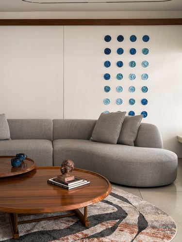 Curved grey sofa beneath grid of blue ceramic discs, round wood coffee table in front