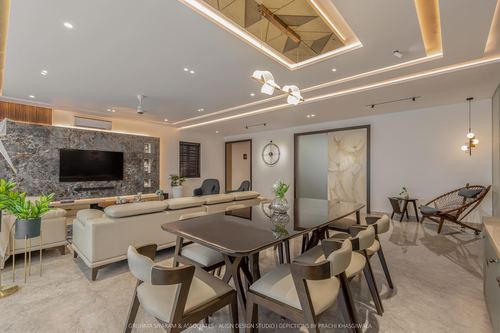 Open-plan living and dining room with marble accent wall, dining table, and layered ceiling lighting
