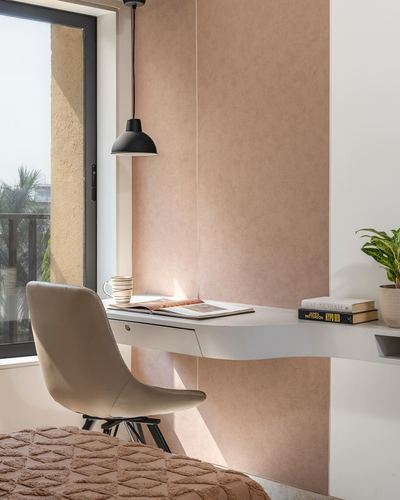 Floating desk with cane chair beneath pendant light against blush textured wall near window