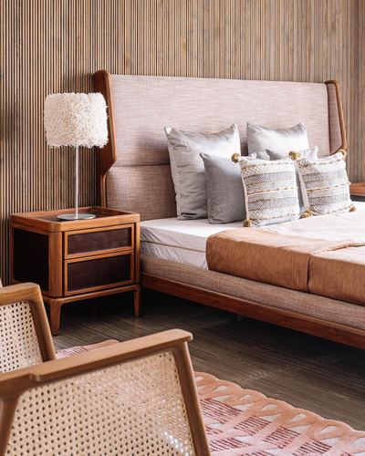 Wooden bedroom with slatted wall, blush headboard, cane chair and carved bedside table