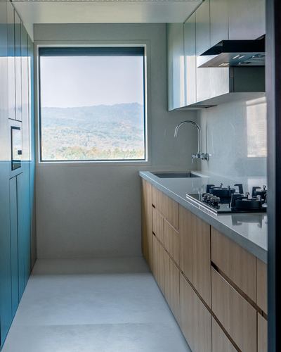Narrow galley kitchen with wood cabinetry and stone counter, framing a forest hill view through a window