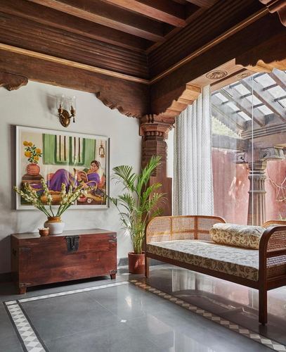 Foyer with cane daybed, wooden trunk, and carved beams beside a glass courtyard wall