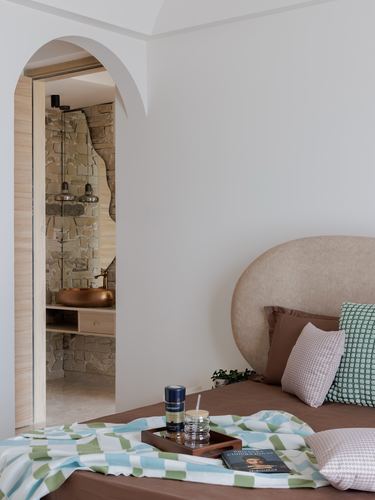 Bedroom with arched doorway revealing stone bathroom, rounded upholstered headboard and patterned throw