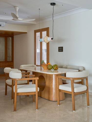 Wood dining table with sculptural pedestal base surrounded by cream armchairs under playful pendant lights