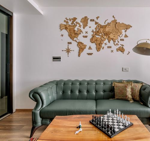 Green tufted chesterfield sofa below a carved wooden world map, chessboard on wood coffee table