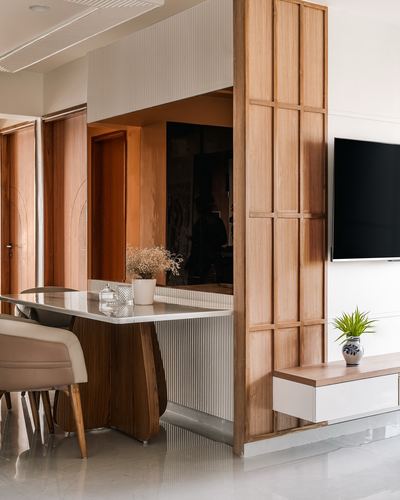 Dining area with marble-top table beside a carved wood lattice partition and wall-mounted tv