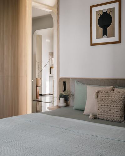 Bedroom corner with upholstered headboard, patterned pillows, and an arched wooden doorway to a vestibule