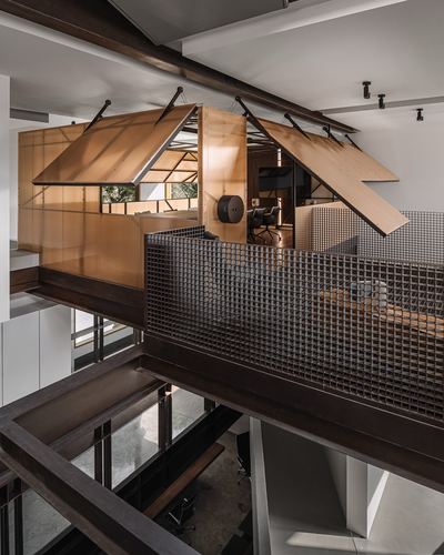 Angular wooden canopy structure above a mesh-railed steel bridge overlooking a void below