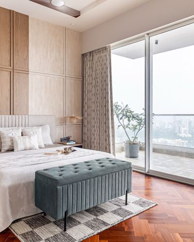 Bedroom with herringbone wood floor, teal tufted bench, and glass door opening to city balcony