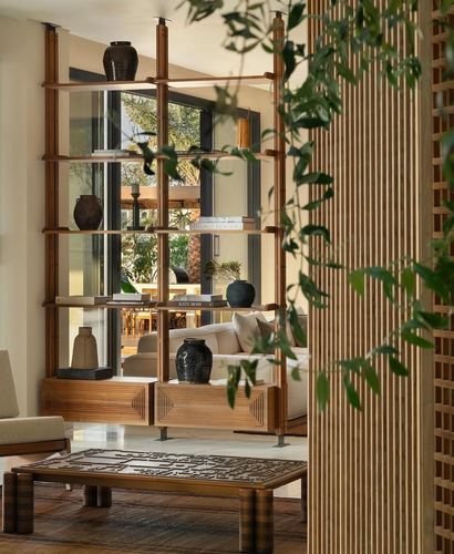 Wooden shelving unit with ceramic vases frames a living room seen beyond, trailing plant in foreground