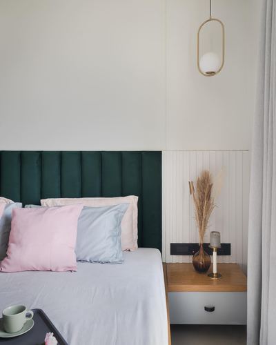 Bedroom corner with green tufted headboard, pastel pillows, and brass pendant light over floating nightstand