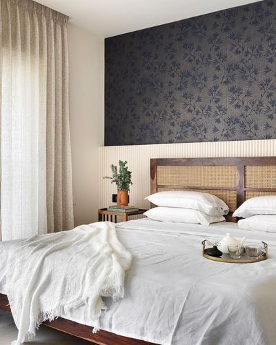 Bedroom with navy floral wallpaper, fluted panel wainscot, cane headboard and white linens