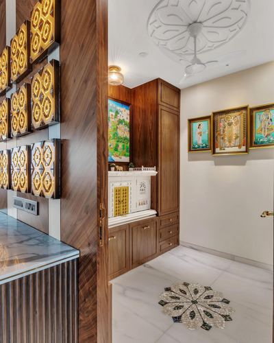 Pooja room nook with white mandir, framed deity paintings, marble floor medallion, and backlit wood wall panels