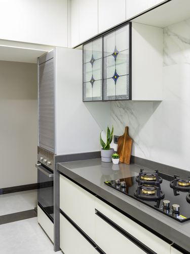 White modular kitchen with stained glass cabinet, marble-look backsplash, and black gas hob on grey countertop