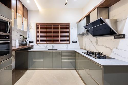 Modern L-shaped kitchen with marble backsplash, grey-green cabinetry, wooden slat window and angled chimney hood
