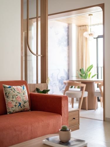 Terracotta sofa in foreground with wood slat divider opening to sunlit dining nook beyond