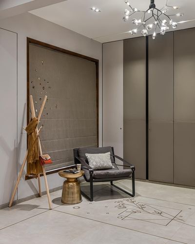 Foyer with fabric pinboard, wooden coat stand, grey armchair, brass table and closet wall