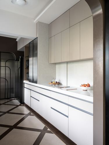 Straight galley kitchen with white cabinetry, taupe upper units and a dark arched doorway frame
