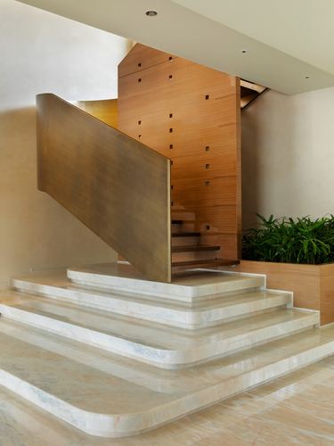 Curved brass staircase balustrade rising beside a perforated wood wall over marble steps