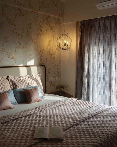 Bedroom with floral wallpaper, chandelier, and quilted pink bedding beside a patterned curtain