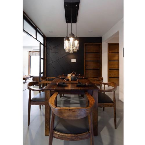Wooden dining table with curved chairs under cluster pendant lights against a black panelled wall