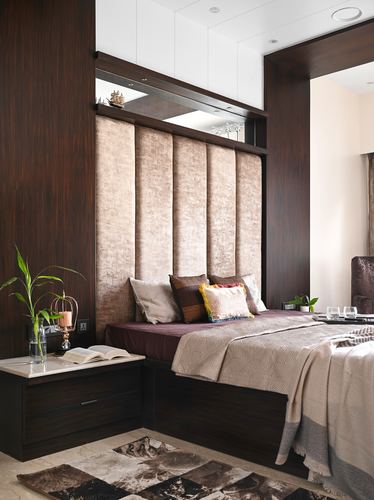 Bedroom with tall upholstered headboard panels, dark wood surround, layered bedding, and marble-top nightstand