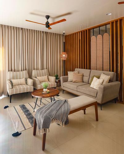 Beige living room with striped armchairs, sofa, round wooden table, and slatted wood partition with woven panels
