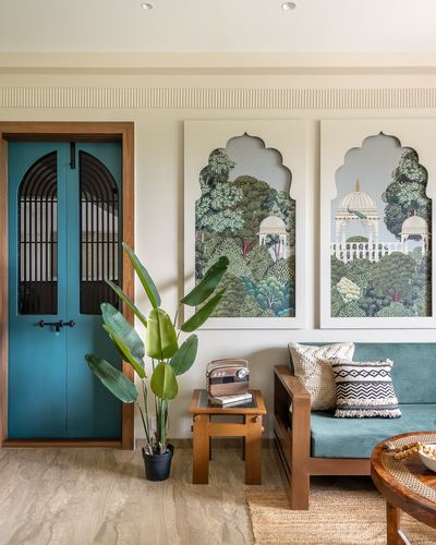 Living room corner with teal arched door, mughal garden art panels, and teak cane sofa