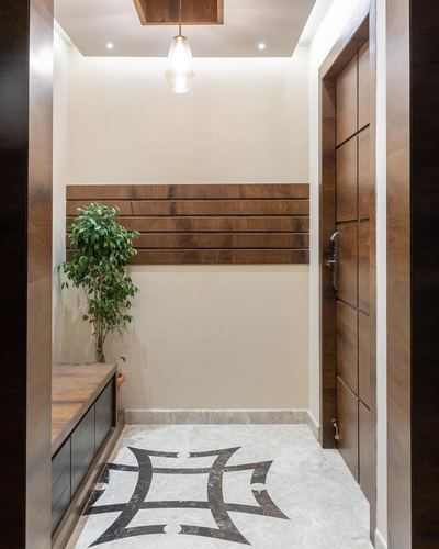 Entryway foyer with slatted wood wall panel, potted plant, console, and inlaid stone floor medallion facing a wooden door