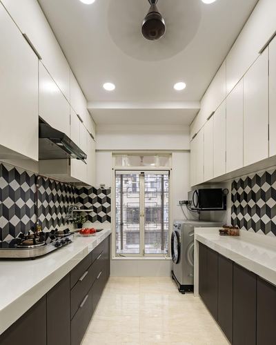 Galley kitchen with black-and-white geometric backsplash, white countertops, dark cabinetry and window at end
