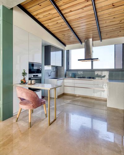 Modern kitchen with wood-slat ceiling, glossy white cabinetry, and pink velvet chair at small table