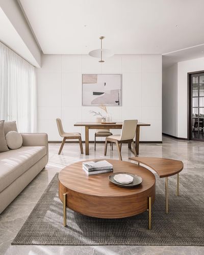 Open living-dining space with round wood coffee table, beige sofa, and dining set against white paneled wall