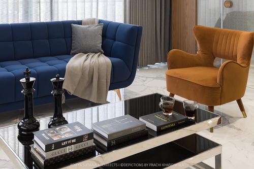 Navy tufted sofa and mustard velvet armchair around a glass coffee table with books and chess pieces