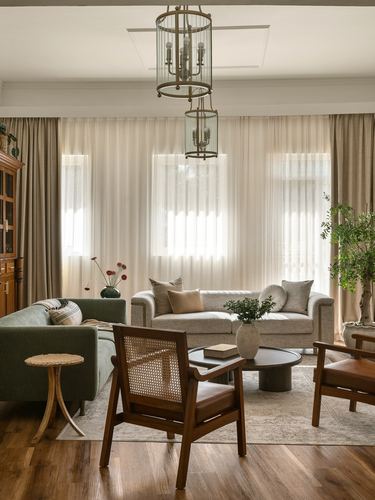 Living room with cane armchairs, green sofa, and layered lantern chandeliers by sheer-curtained windows